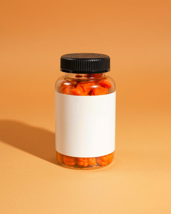 A clear bottle filled with orange gummy vitamins against an orange background.